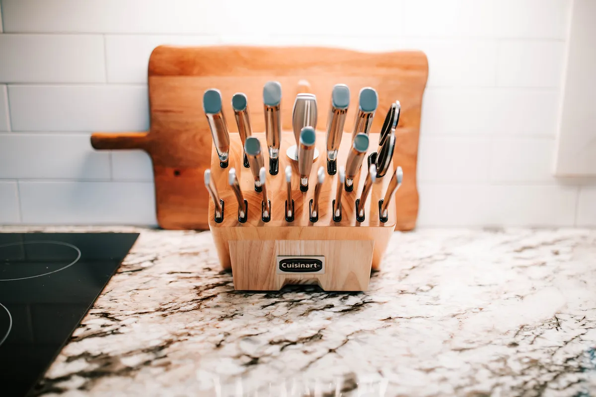 A close-up view of a marble countertop with a knife block, cooking utensils, and a cutting board, spotlighting the functional aspect of the kitchen. The modern and organized setup is ideal for meal prep or culinary adventures.