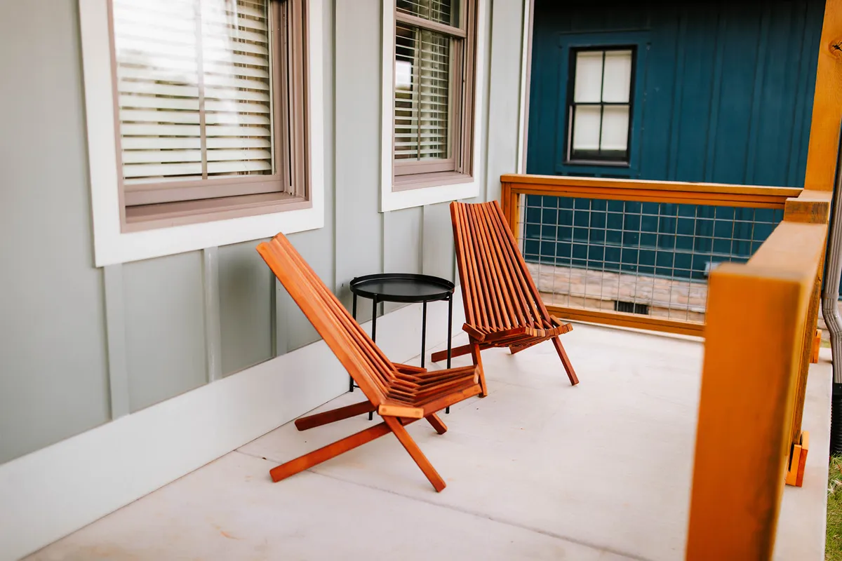 This exterior image captures two wooden lounge chairs and a small round table set against a textured wall. The chairs face outward, suggesting a peaceful spot for sunrise views, sunset watching, or stargazing. The mood is calm and serene, evoking the intimate moments that define a romantic escape.