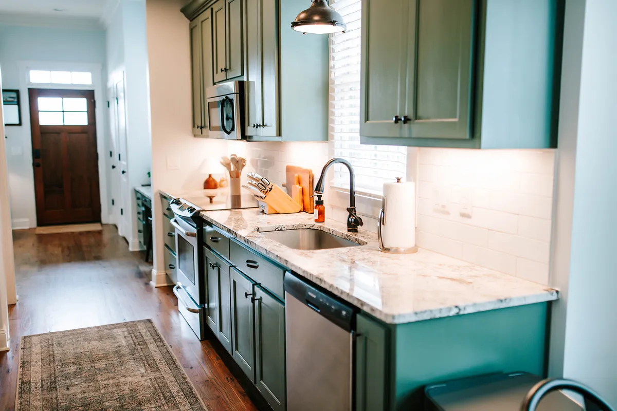 Another inviting kitchen view showcasing green cabinetry, a granite countertop, a modern kitchen sink, and quality appliances. The warm ambiance suggests it's perfect for group gatherings, celebrations, or quiet culinary moments.