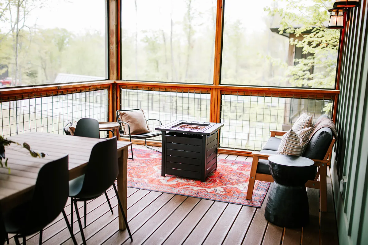 A cozy, semi-outdoor seating area centered around a fire pit, with a decorative rug and wooden walls. Plush chairs invite relaxation, socializing, or enjoying a warm drink. The space suggests opportunities for intimate evenings spent together in comfort, blending indoor and outdoor elements.
