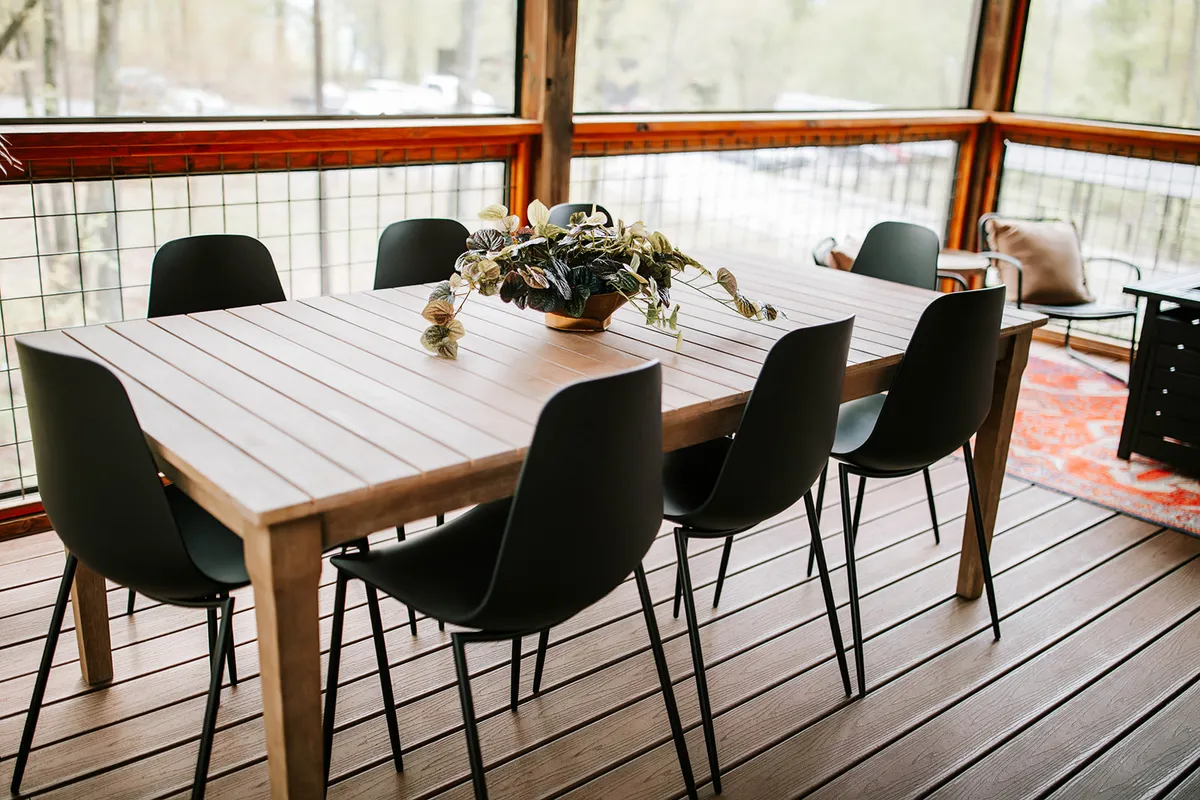 A bright and inviting dining area featuring a wooden table, black chairs, and a vibrant floral centerpiece. The space is filled with natural light, highlighting an atmosphere ideal for group gatherings, celebratory meals, or intimate conversations.