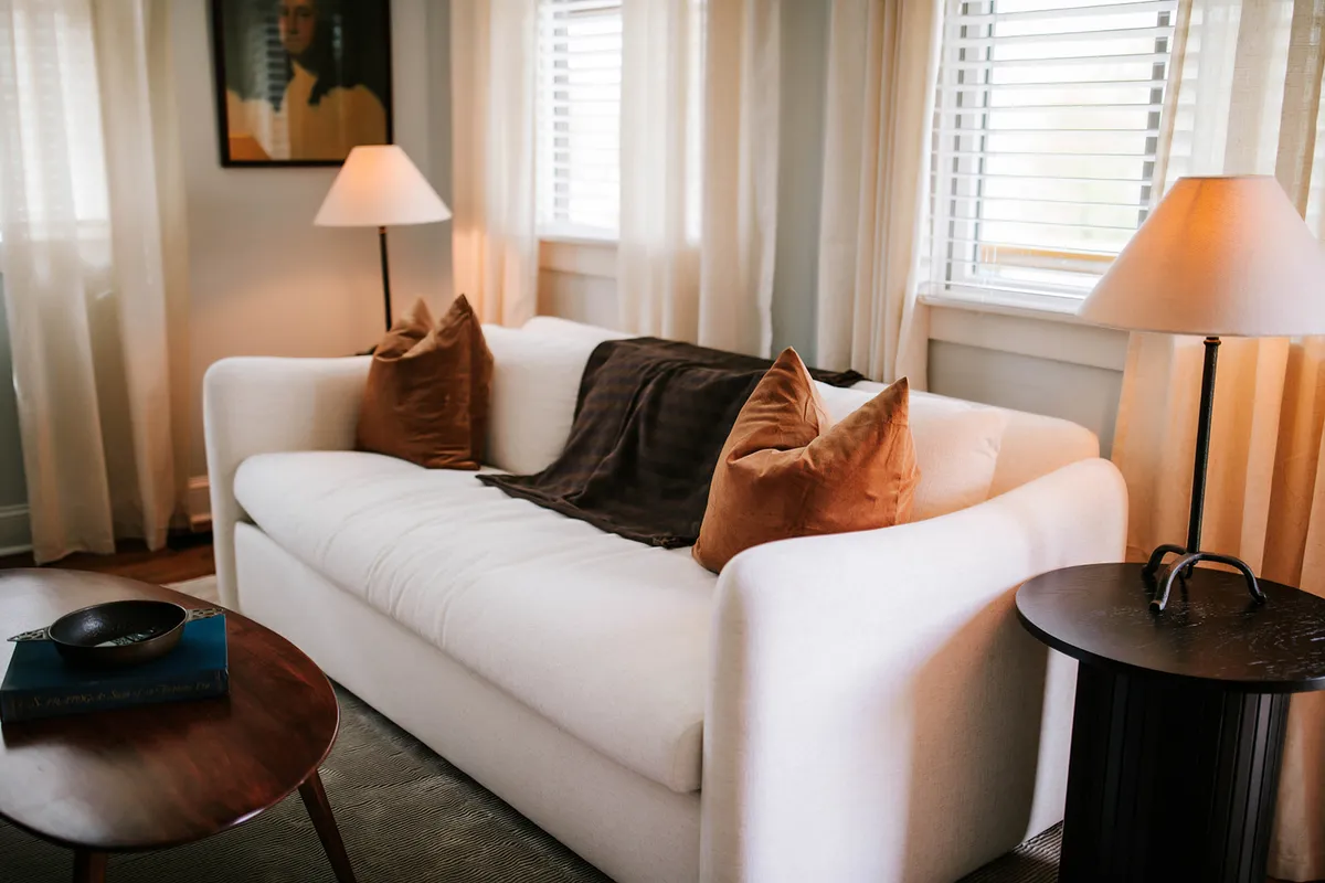 A cozy seating area with a sofa adorned with decorative pillows, warm table lamps, and a side table. The soft lighting and ample seating create a warm, welcoming atmosphere for socializing or relaxing.
